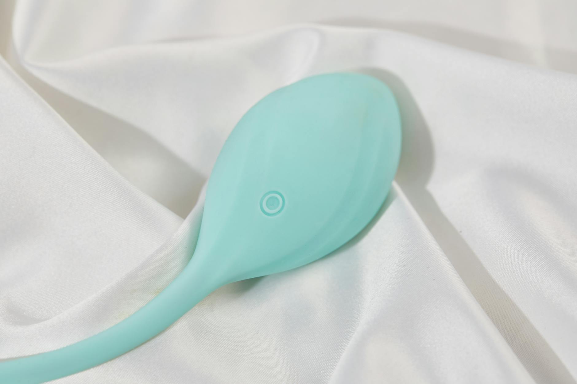 A sleek teal lemon vibrator on smooth white silk fabric, symbolizing sensuality and modern intimacy for mature adults.