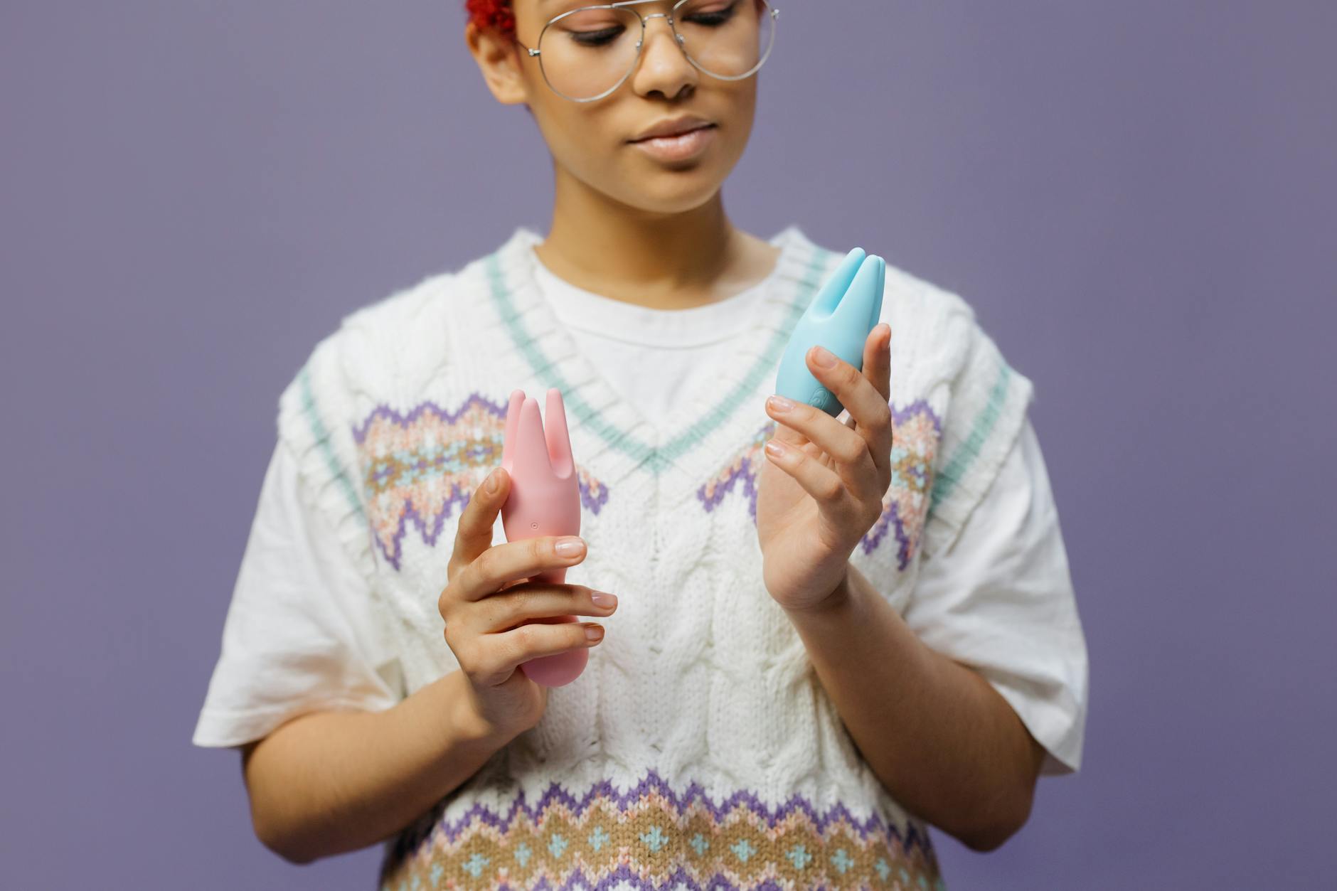 Woman holding blue and pink clitoral vibrators while considering her options during recovery.